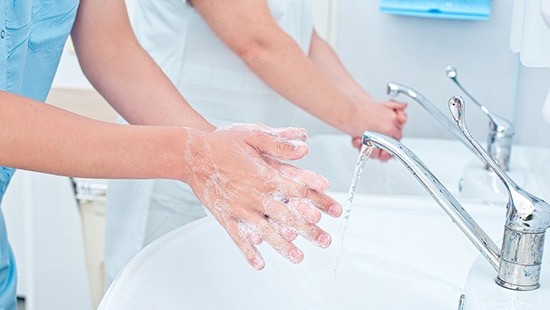 Healthcare workers practicing Ecolab Hand Hygiene Program by washing hands over the sink.